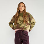 Model i grøn camouflage pullover med høj krave og hænderne på hofterne, tæt på forfra