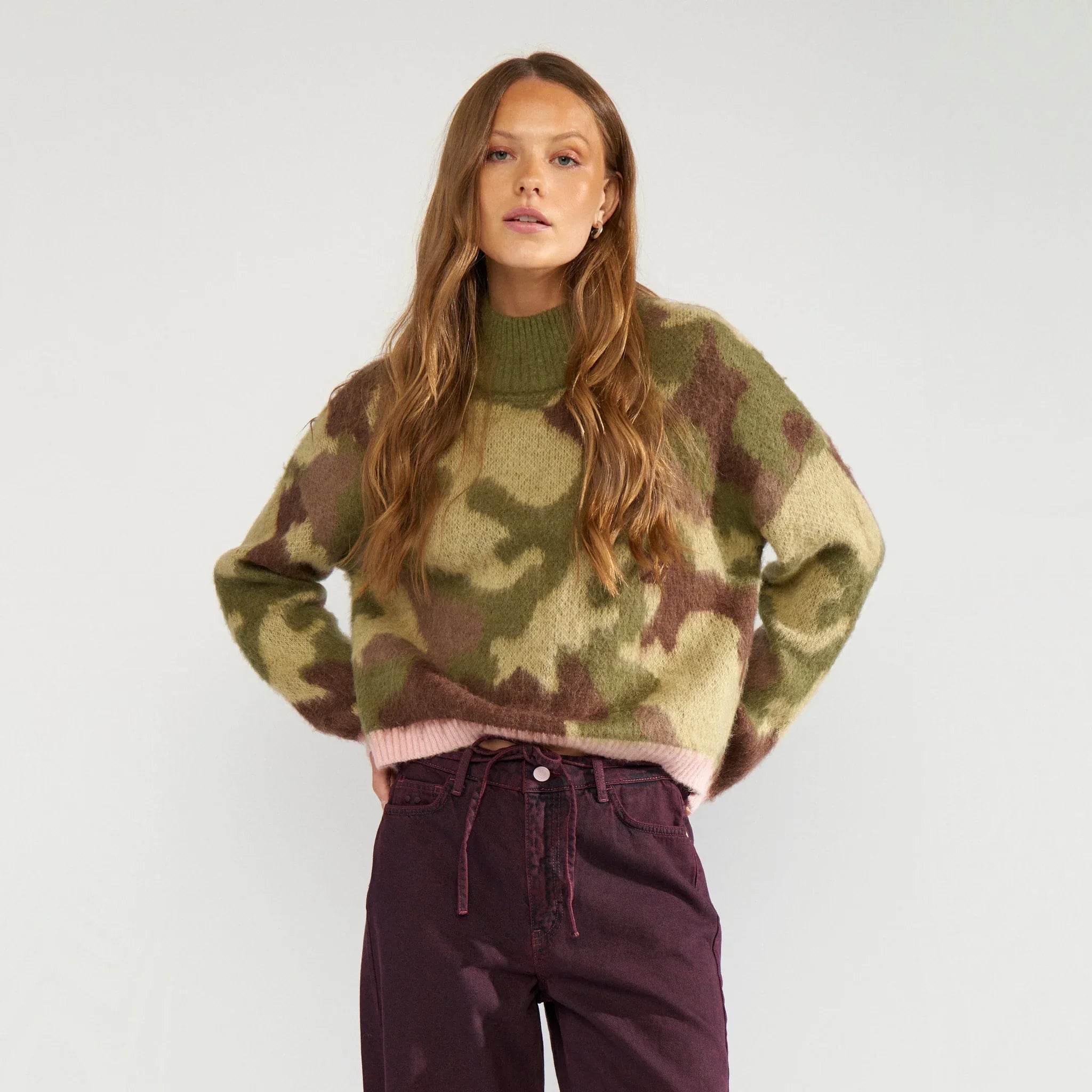 Model i grøn camouflage pullover med høj krave og hænderne på hofterne, tæt på forfra