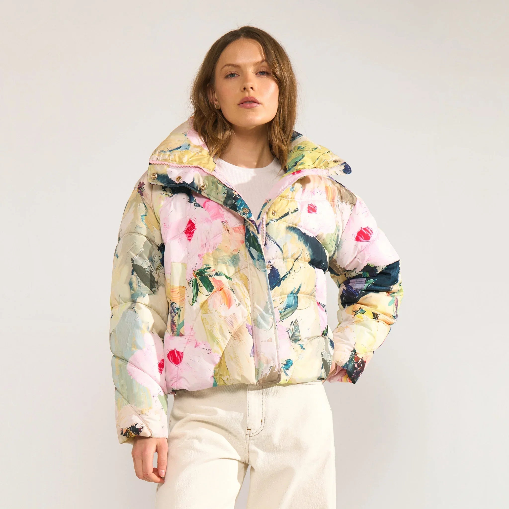 Model i kort pink pufferjakke med print, åben krave, lynlås og trykknapper, sammen med hvide jeans