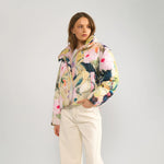 Model i hel figur i kort pink pufferjakke med print, lyse jeans og brune sneakers