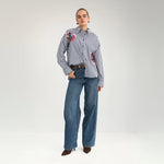 Model i hel figur i stribet oversize skjorte med to broderede blomster, stylet med vide jeans