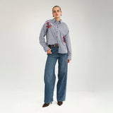 Model i hel figur i stribet oversize skjorte med to broderede blomster, stylet med vide jeans
