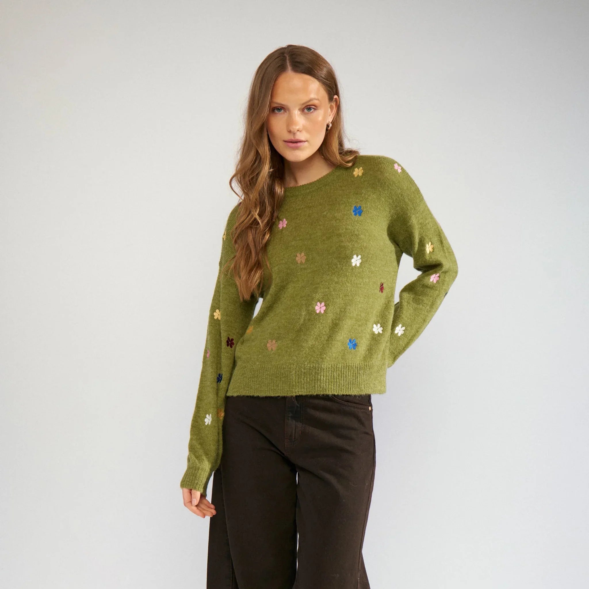 Model i grøn pullover med broderede blomster, stylet med brune jeans og sneakers, helfigur forfra