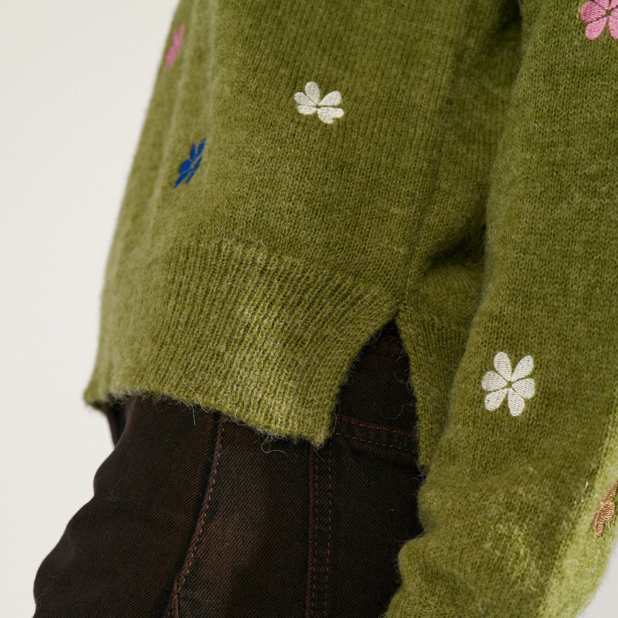 Nærbillede af slids i siden, ribkant og ærme på grøn pullover med broderede blomster