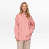 Model i rød stribet oversize skjorte med lange ærmer og beige bukser, forfra