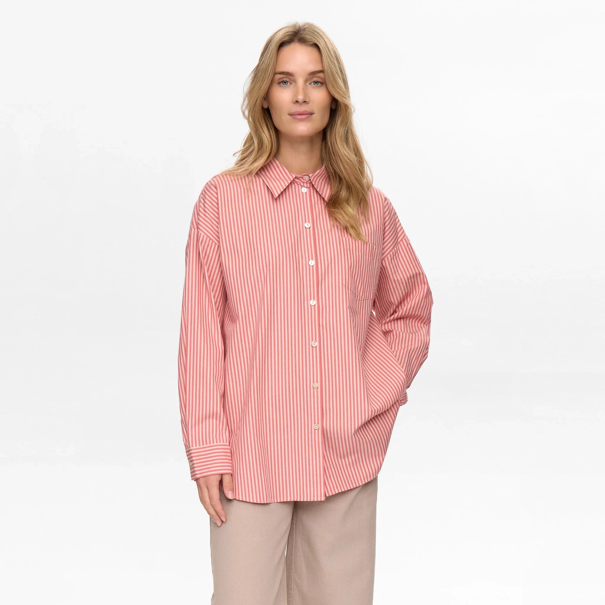 Model i rød stribet oversize skjorte med lange ærmer og beige bukser, forfra