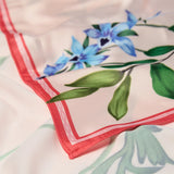 Nærbillede af hjørnet på pink satin tørklæde med blå blomster, grønne blade og rød kant