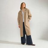 Model i åben lang beige jakke med stribet skjorte og wide leg jeans, set forfra