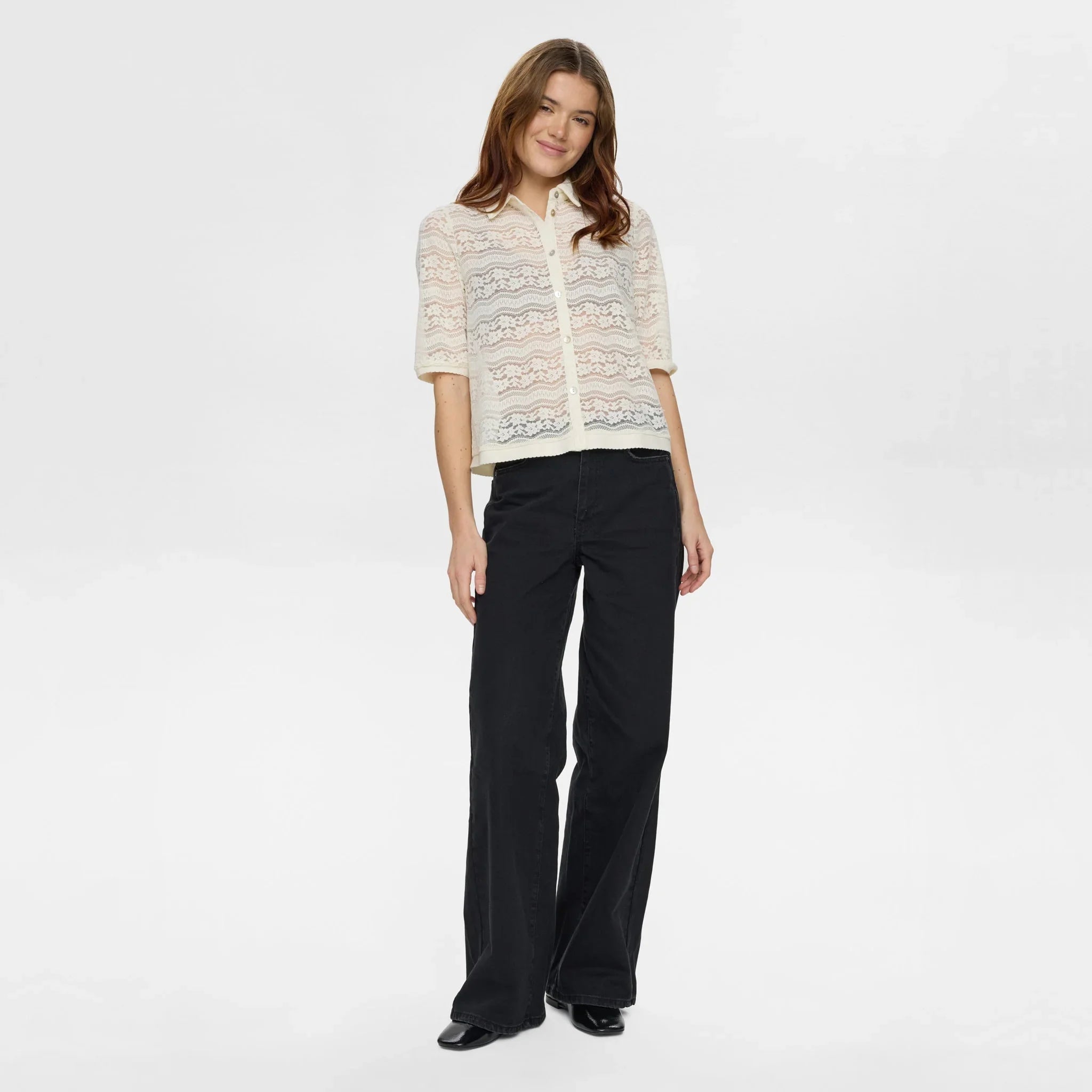 Model i hvid blondeskjorte med sorte vide jeans og sorte sko, hele figuren