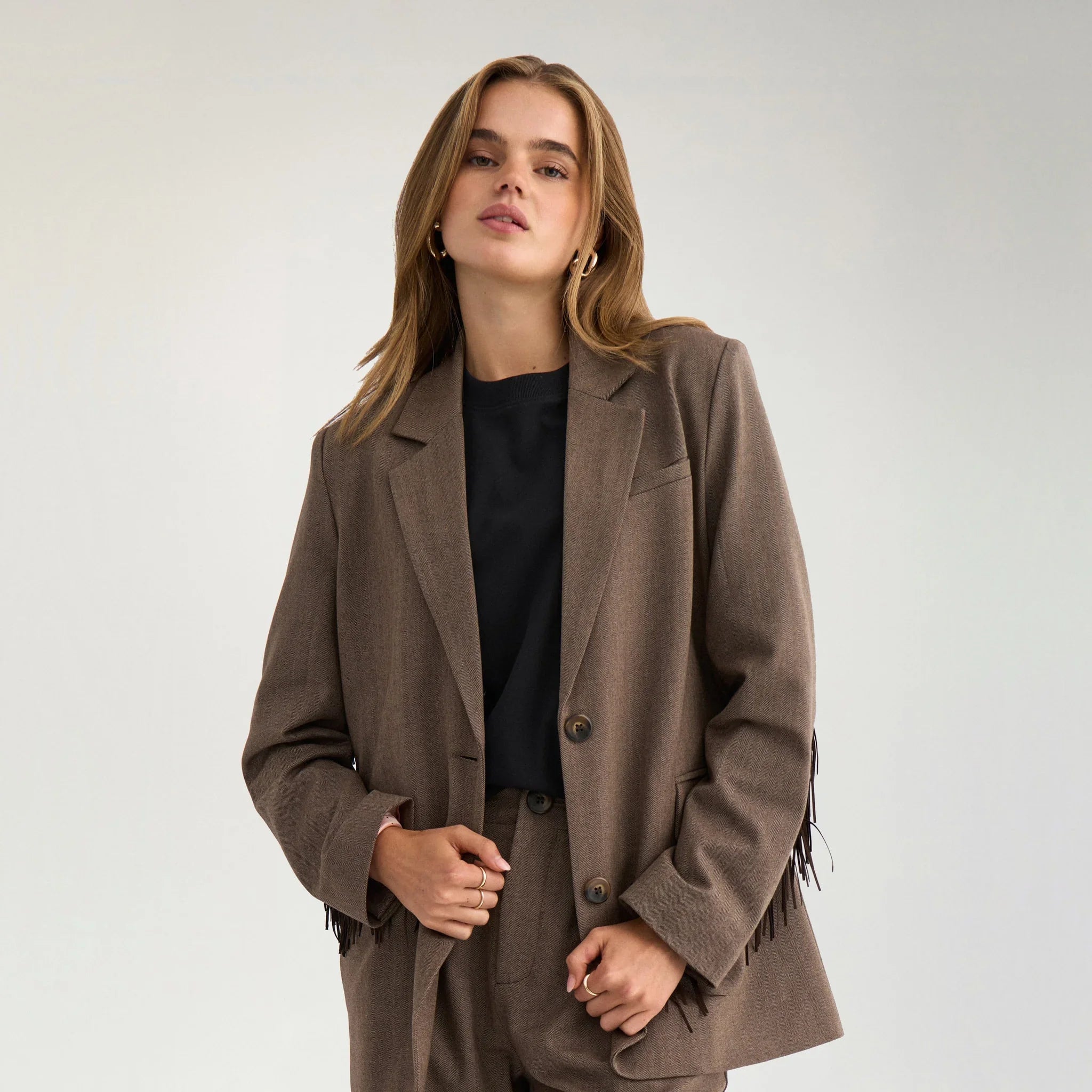 Model i brun blazer med frynser over en sort t-shirt, tæt på forfra