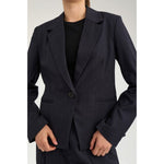 Nærbillede af navy blazer med reverskrave, én knap og lommer foran på model