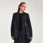 Model i navy oversize blazer med hvide motiver over en sort top, set tæt på forfra