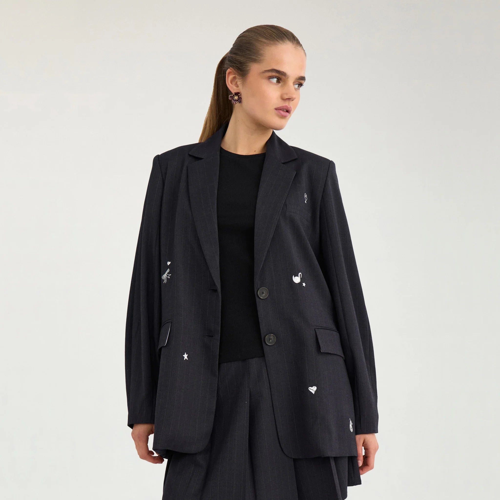 Model i navy oversize blazer med hvide motiver over en sort top, set tæt på forfra