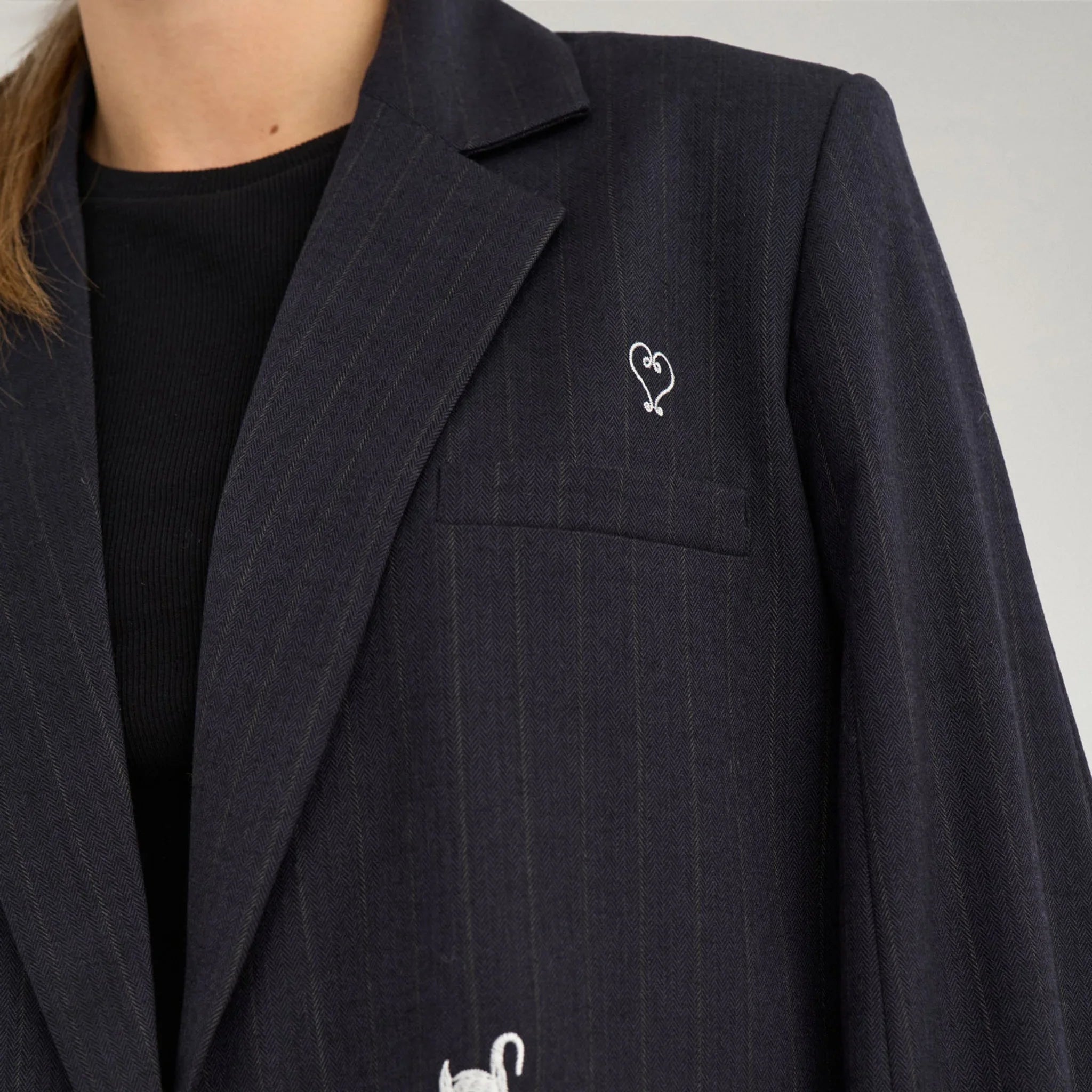 Nærbillede af navy blazer med hvid svane, stjerne og hjerte ved brystlommen