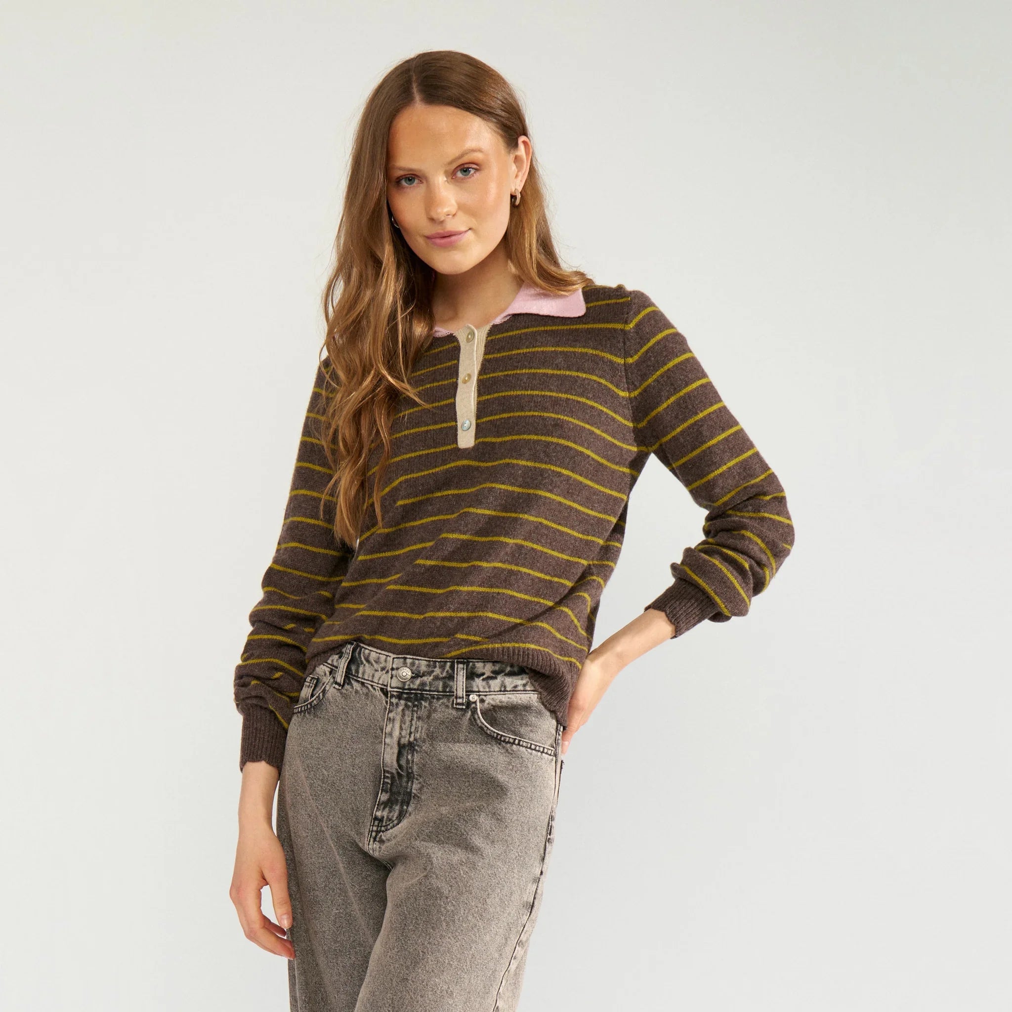 Model i brun stribet pullover med lyserød polokrave og grå jeans, tæt på forfra