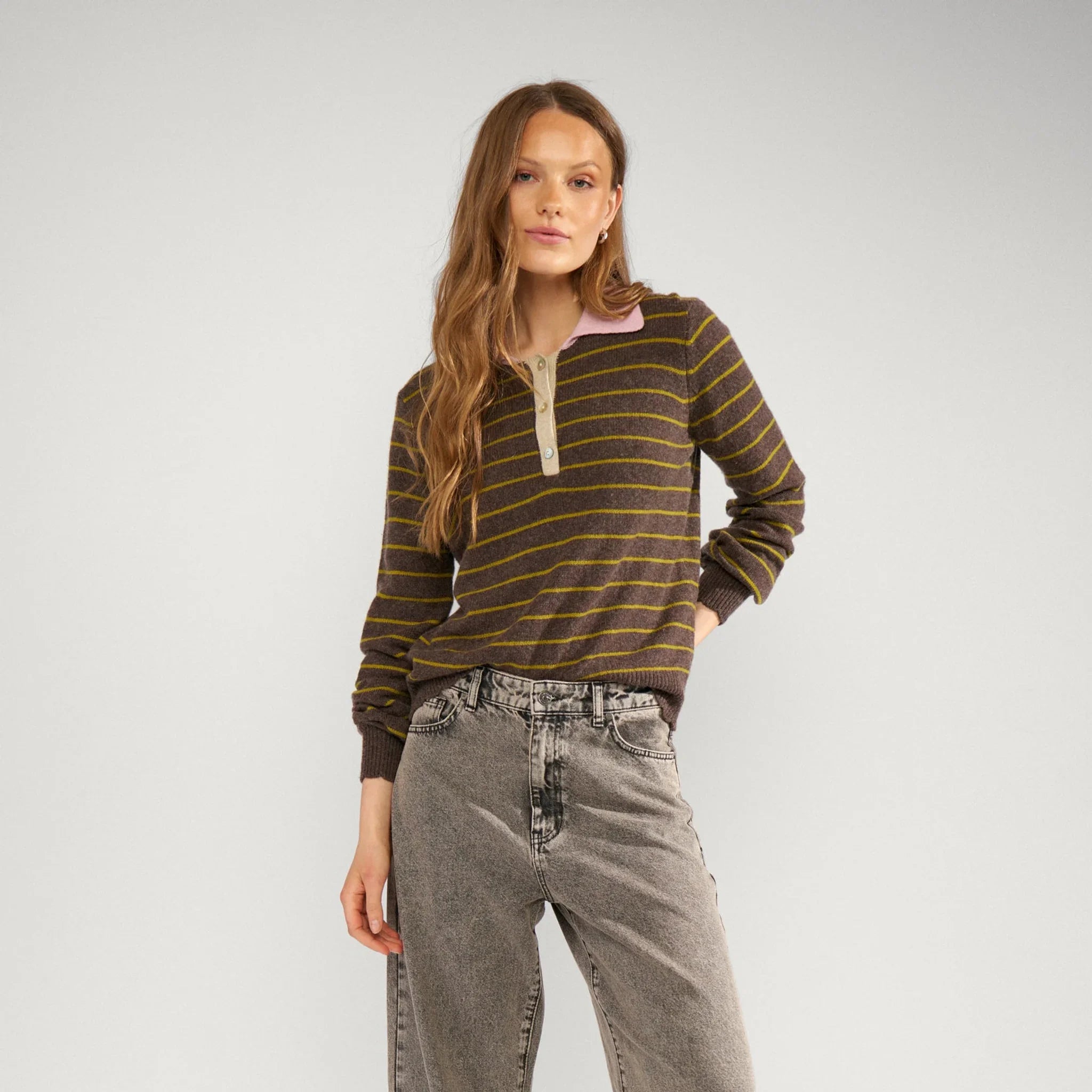 Model i hel figur i brun stribet pullover stylet med grå jeans og sorte loafers