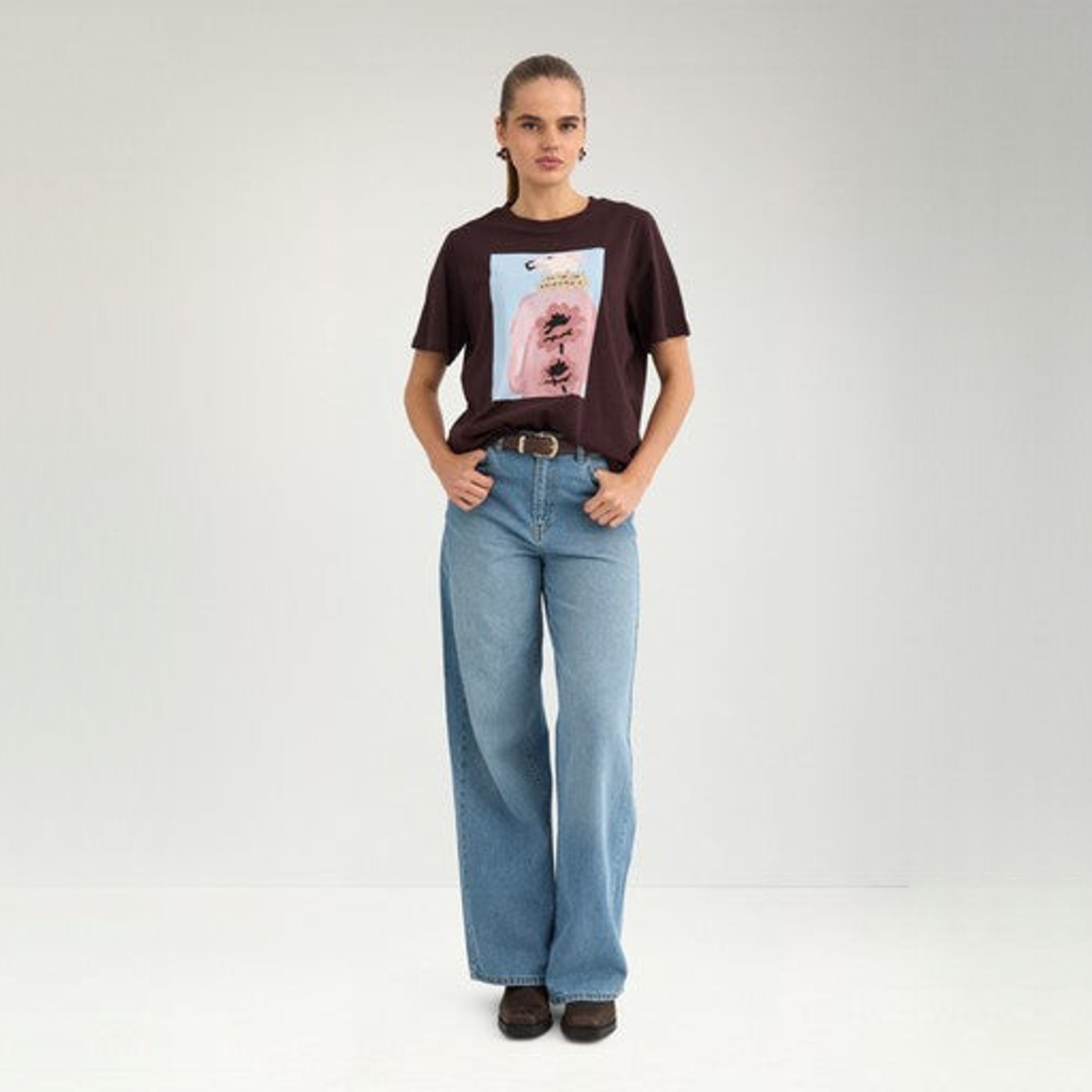 Model i fuld figur i brun t-shirt med print og lyse wide leg jeans