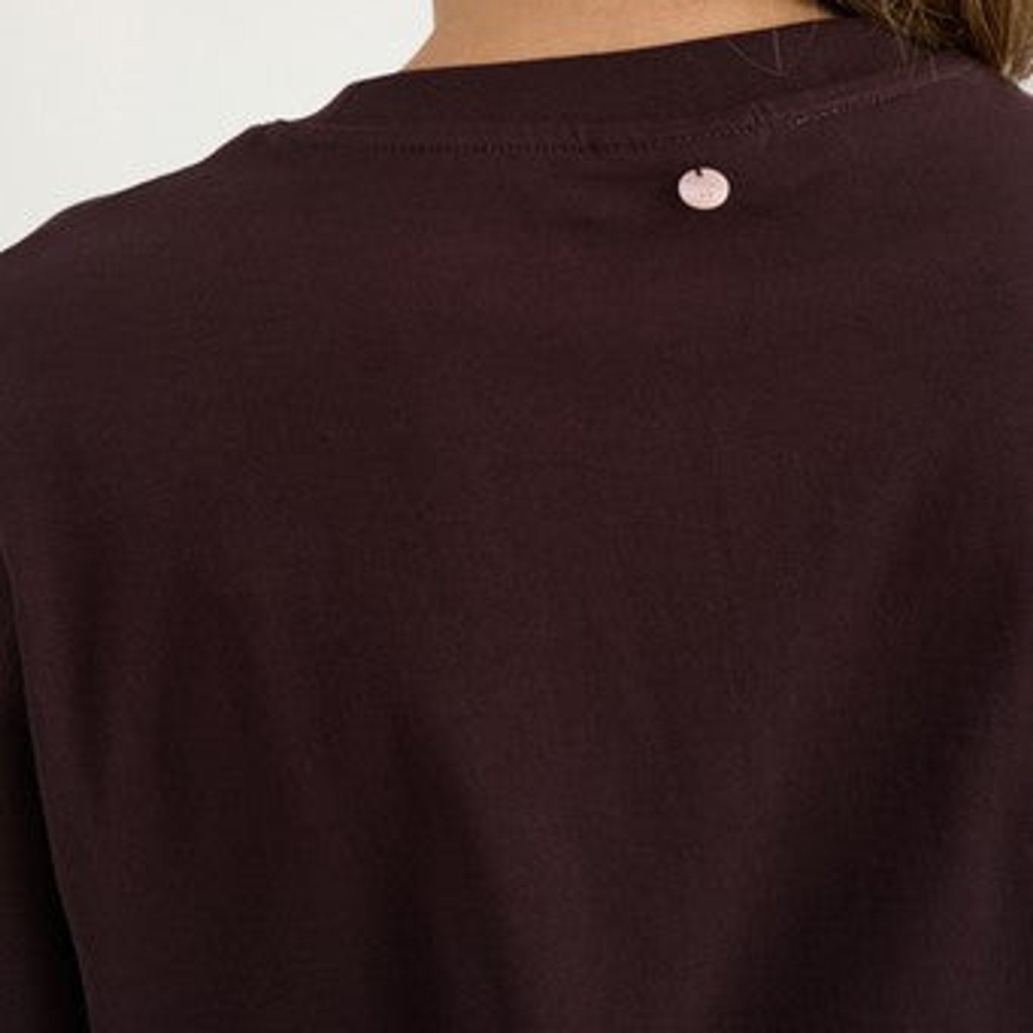 Nærbillede af lyserødt mærke i nakken på brun t-shirt i farven Chocolate Plum