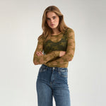 Model i grøn gennemsigtig bluse i blonde og blå jeans med armene over kors