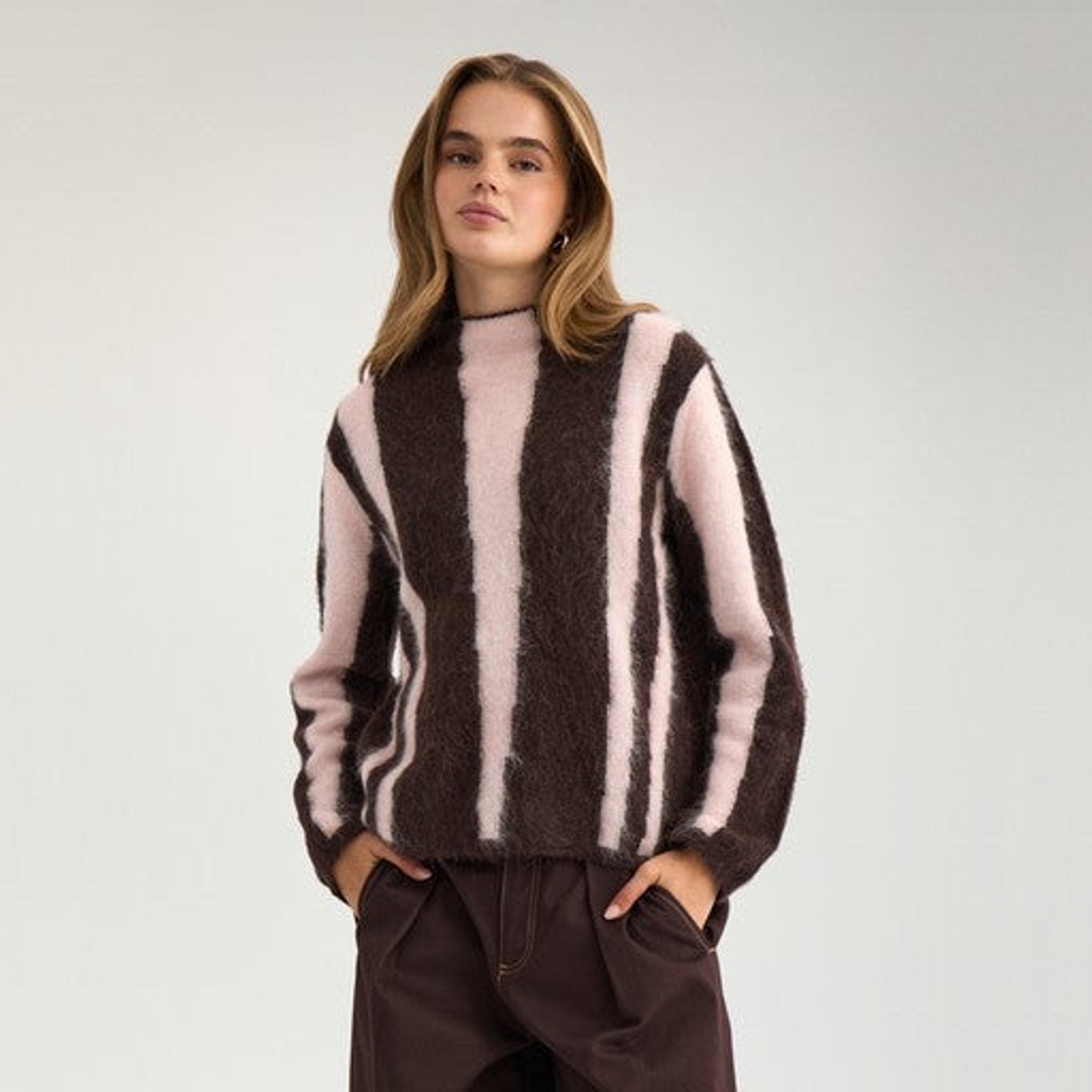 Model i brun pullover med lyserøde striber og brune bukser set forfra