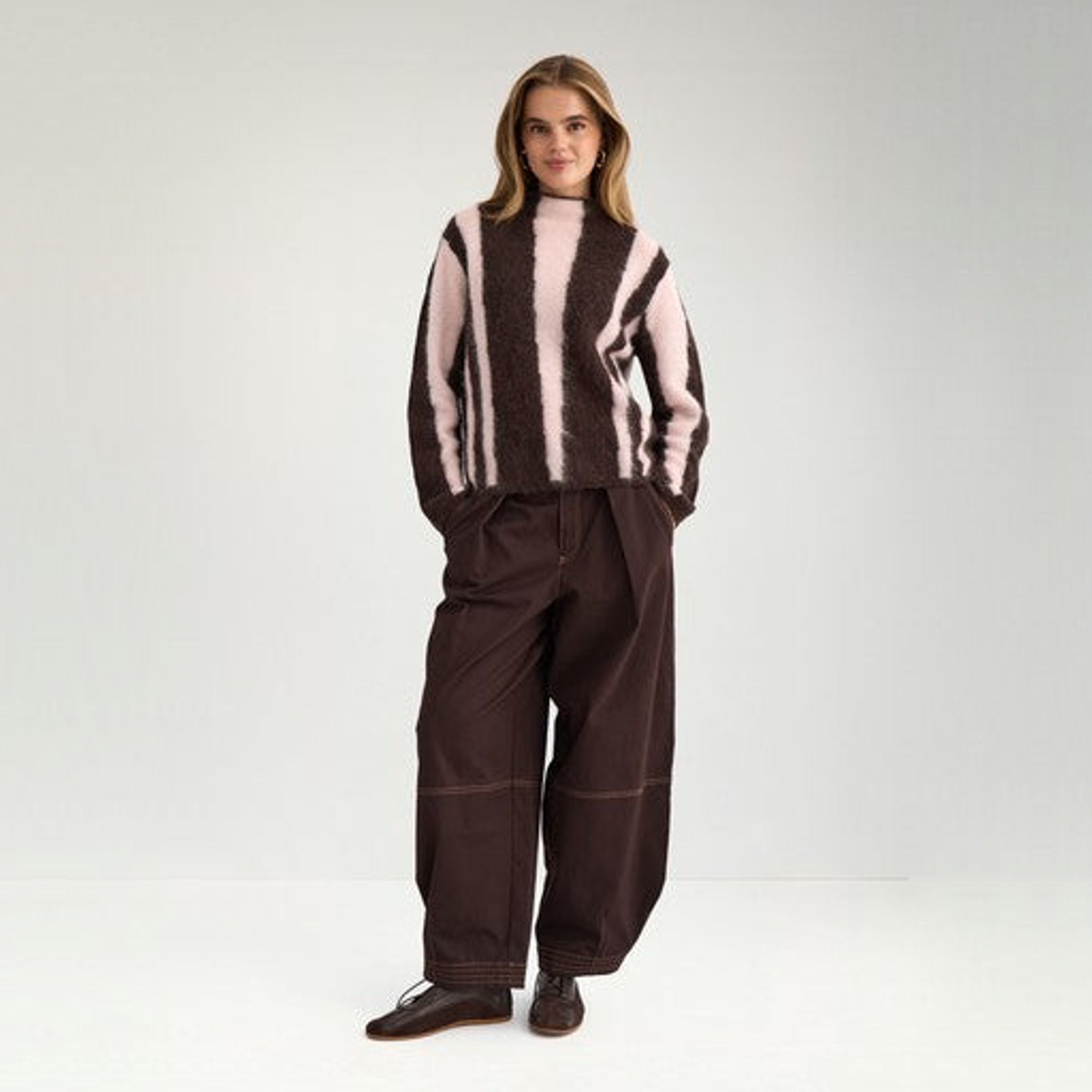 Model i fuld figur i brun stribet pullover med høj hals stylet med brune bukser