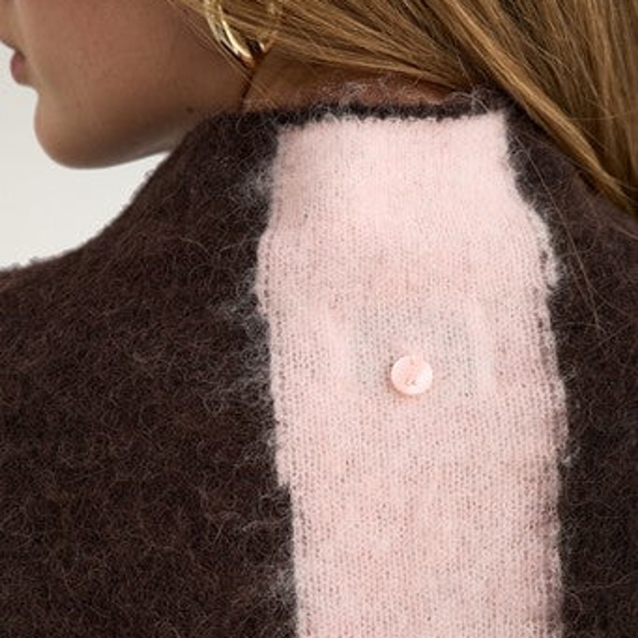 Detalje af lille lyserød knap i nakken på brun stribet pullover