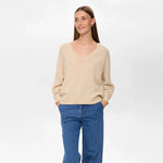 Model i beige pullover med V-hals og blå jeans set forfra