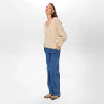 Model i beige pullover med V-hals set fra siden i fuld længde med jeans