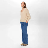Model i beige pullover med V-hals set fra siden i fuld længde med jeans