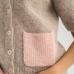 Nærbillede af lyserød lomme i ribstrik og knapper på beige cardigan