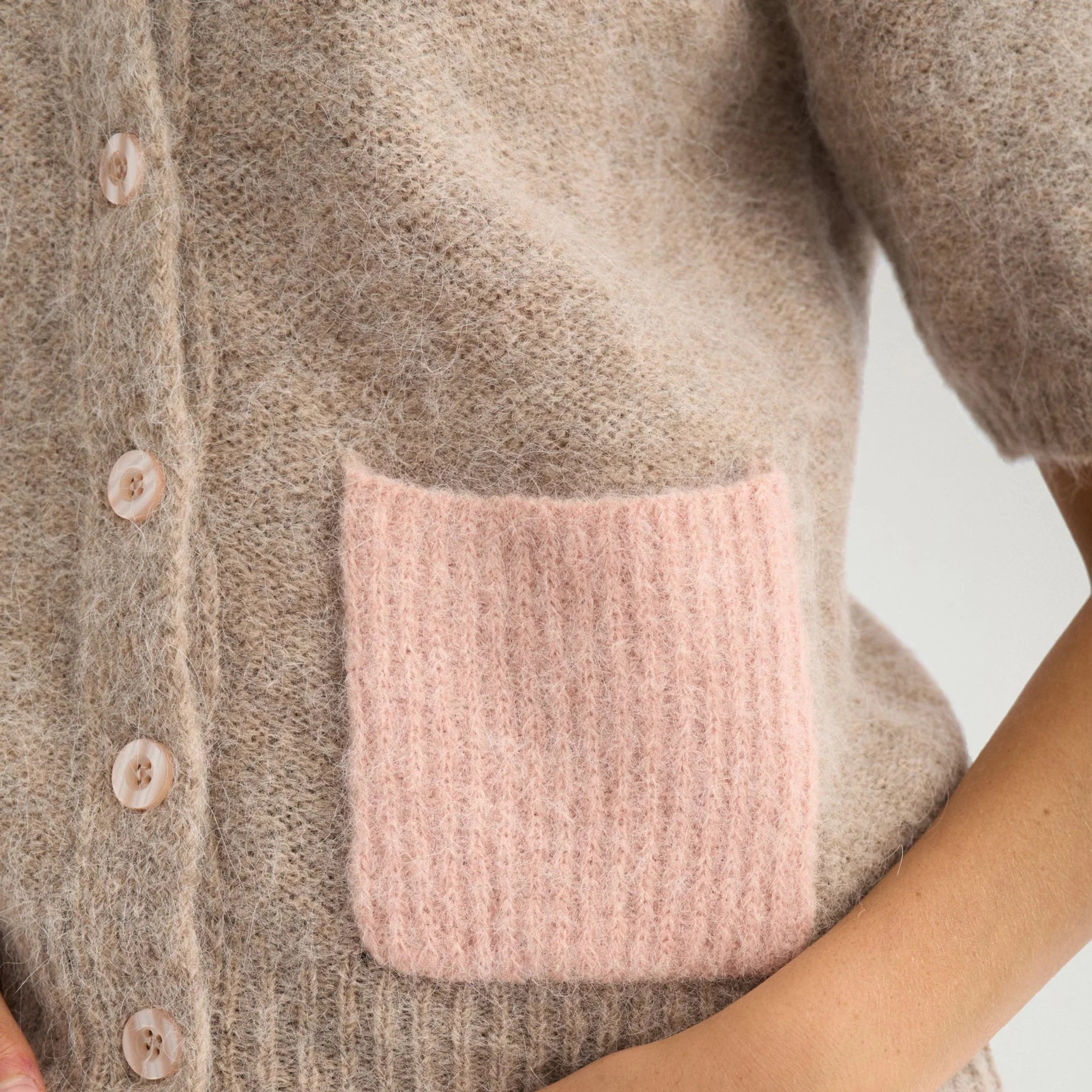 Nærbillede af lyserød lomme i ribstrik og knapper på beige cardigan