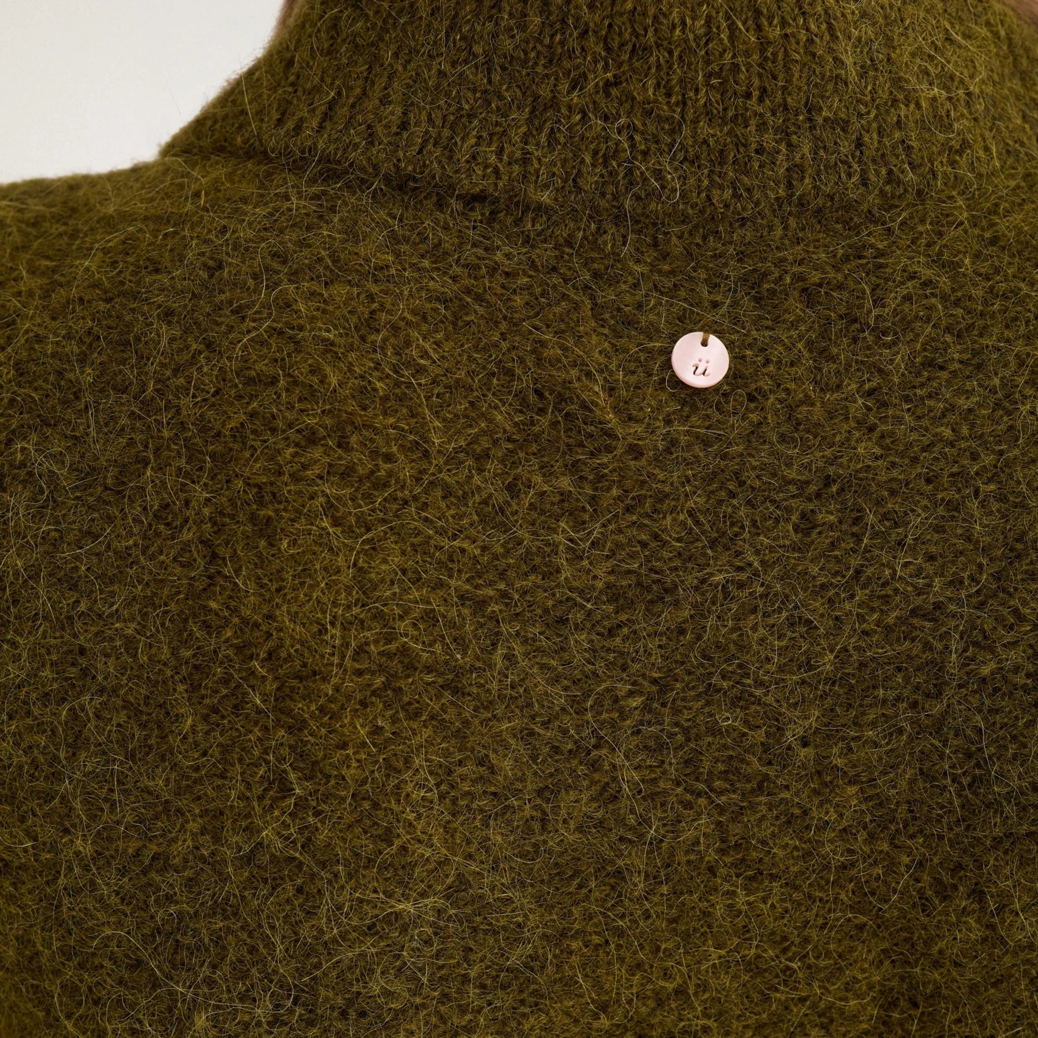 Nærbillede af krave og lille logo bag i nakken på grøn cardigan i fluffy strik