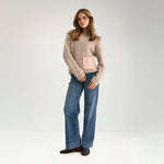 Model i hel figur i beige Nusalia strik i Sesame Melange stylet med blå jeans