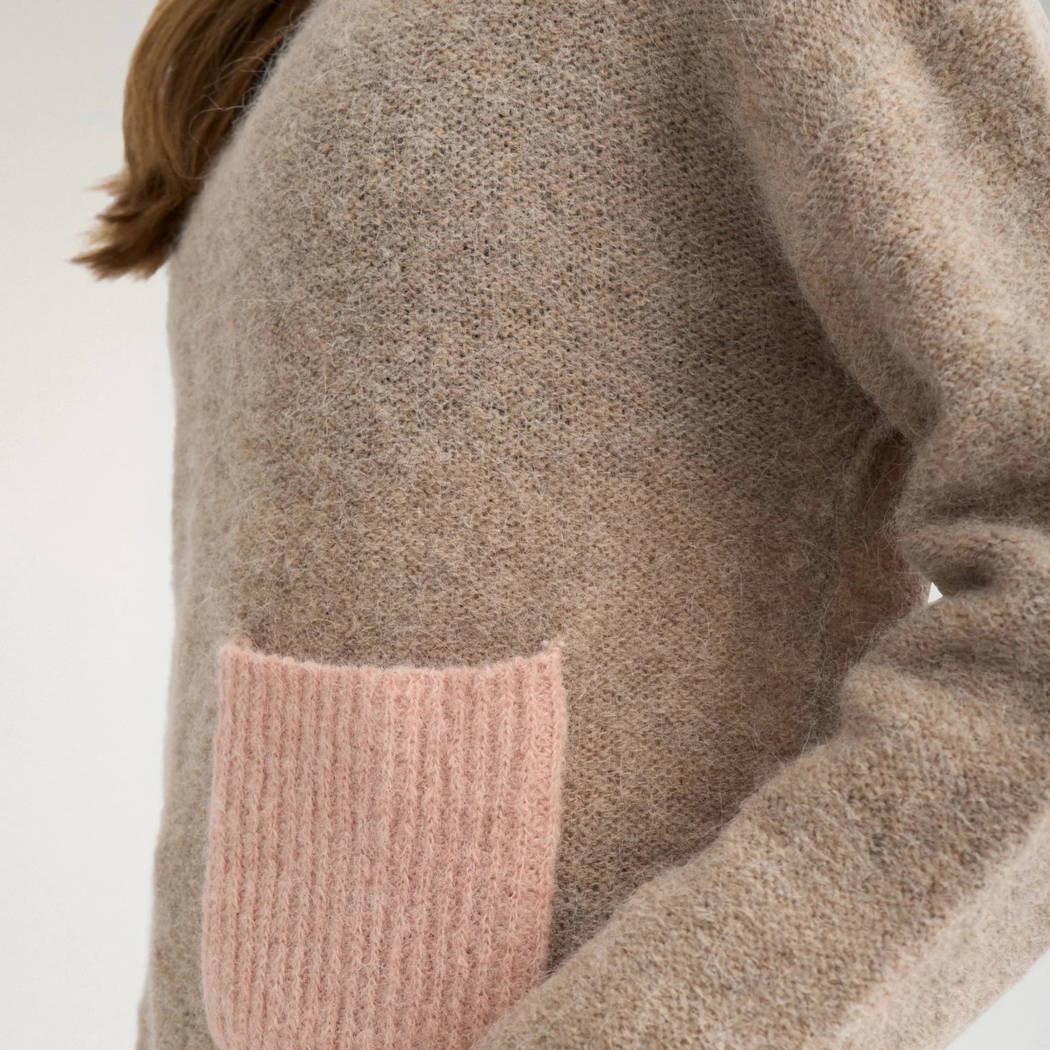 Nærbillede fra siden af lyserød lomme i ribstrik på beige strik i Sesame Melange