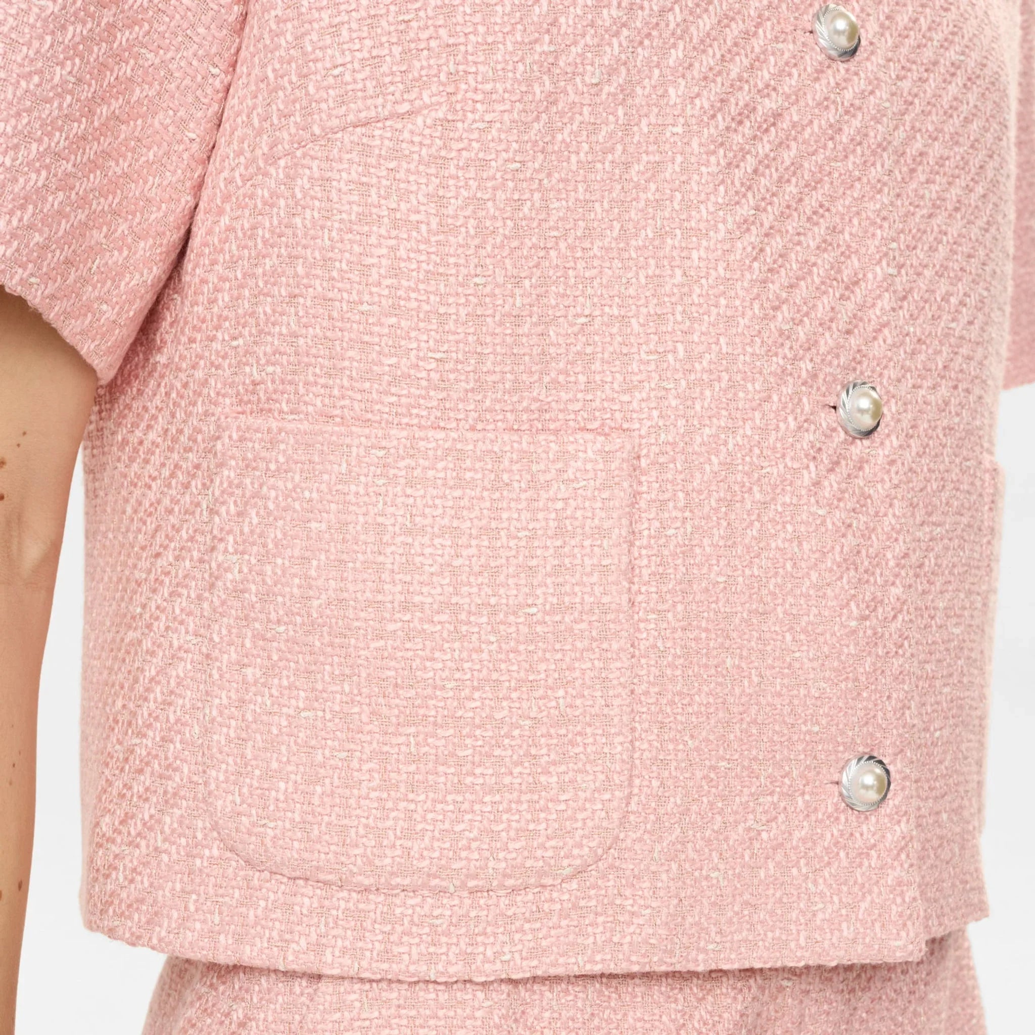 Detalje af pink jakkes vævede stof, påsyet lomme og perlelignende knapper