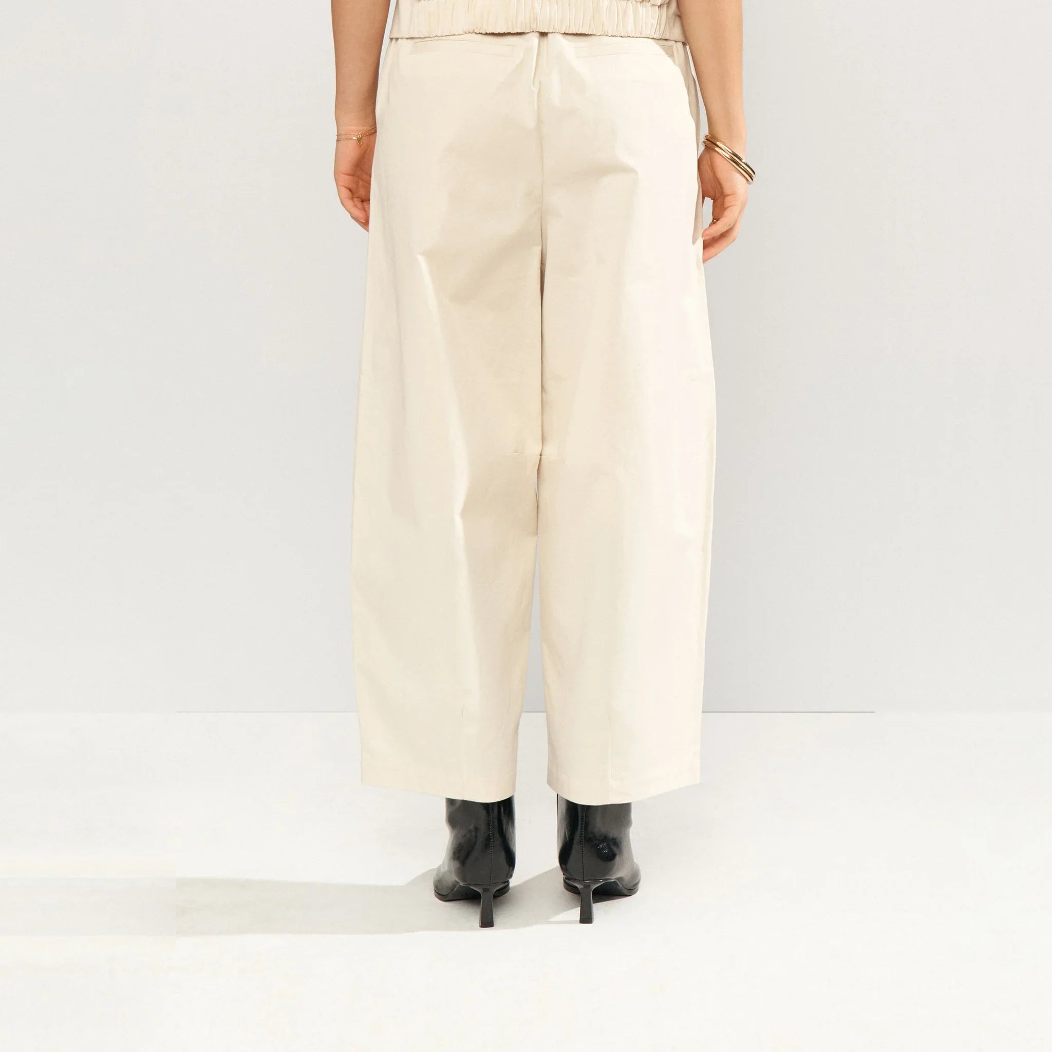 Model i beige wide leg bukser bagfra med sømme ved knæene