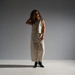 Model i beige wide leg bukser med buet form mod grå baggrund
