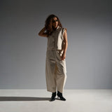 Model i beige wide leg bukser med buet form mod grå baggrund