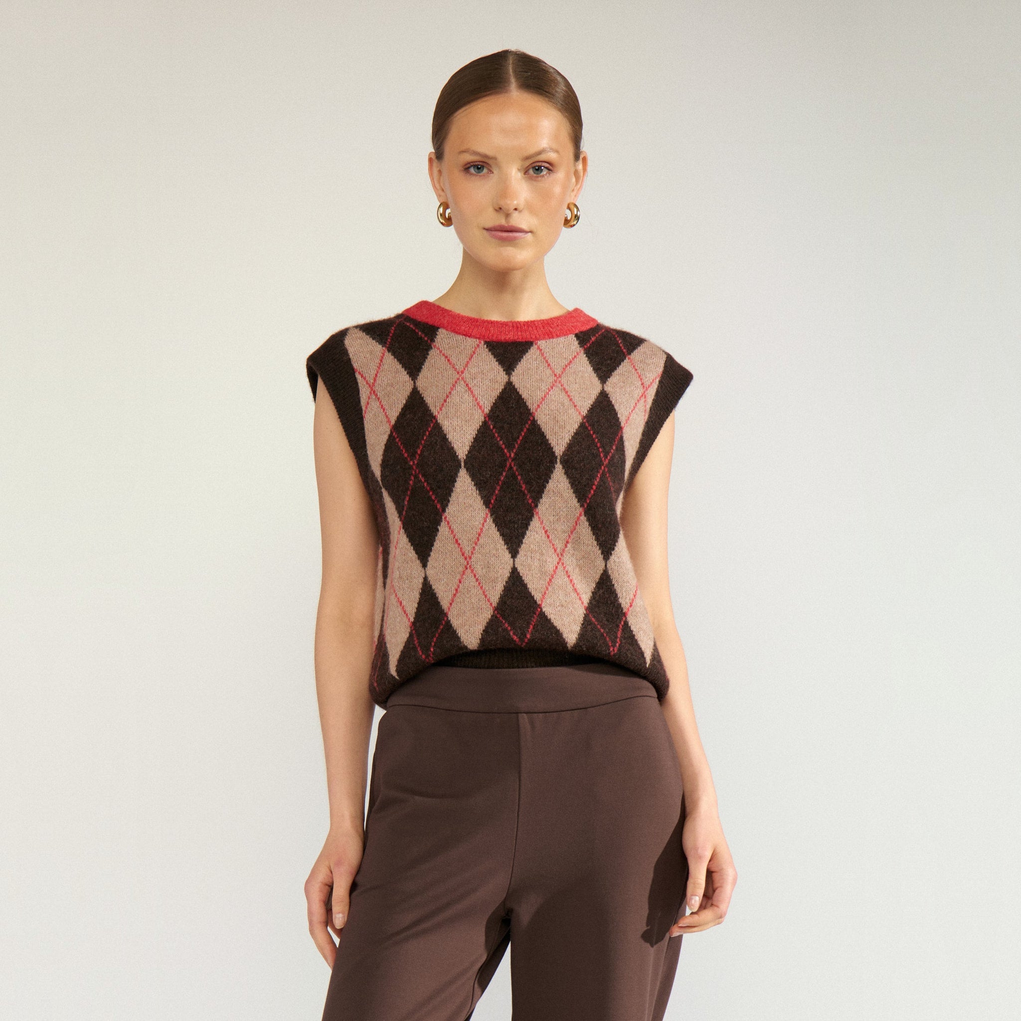 Model i brun og beige argyle vest med rød halskant, stylet med brune bukser, set forfra
