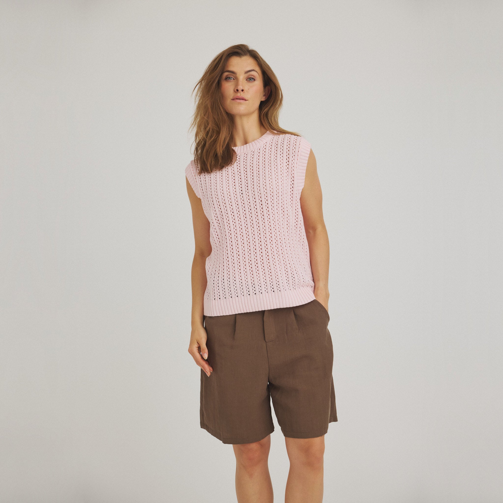 Model i grønne shorts med vide ben og hånd i lommen, stylet med en lyserød strikvest