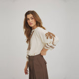 Model i hvid bluse med brune broderier foran og på de puffede 3/4-ærmer, set skråt fra siden