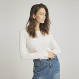 Model i tætsiddende hvid langærmet t-shirt med bølgede kanter ved ærmerne, stylet med denimnederdel