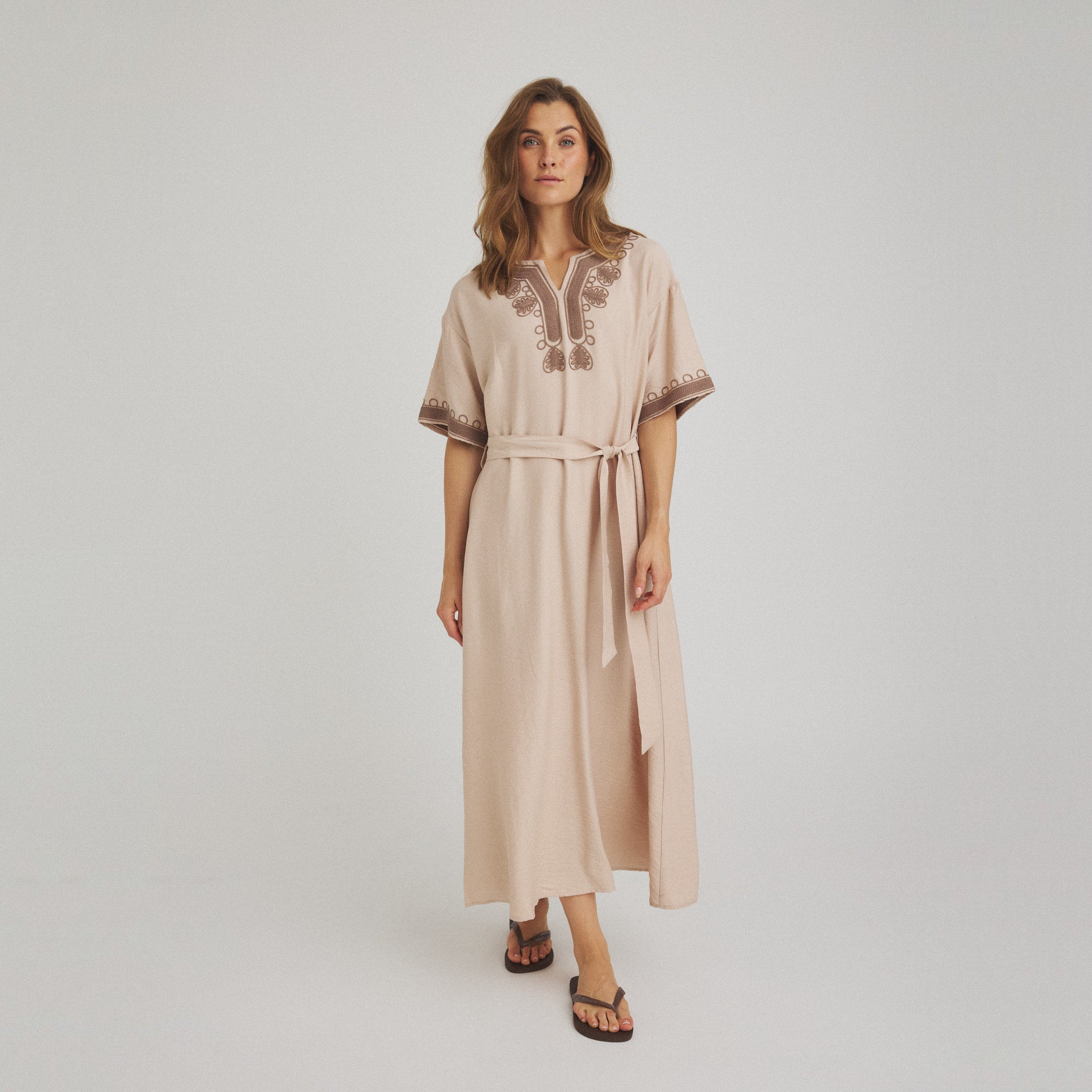 Model i beige Vava Dress kjole fra OneTwo Luxzuz med brune broderier og bindebælte, set forfra