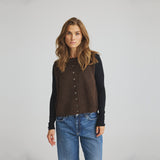 Model i brun strikket vest med knapper over sort langærmet bluse og blå jeans