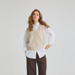 Model i beige vest med perler foran, båret over en hvid skjorte