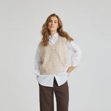 Model i beige vest med perler foran, båret over en hvid skjorte
