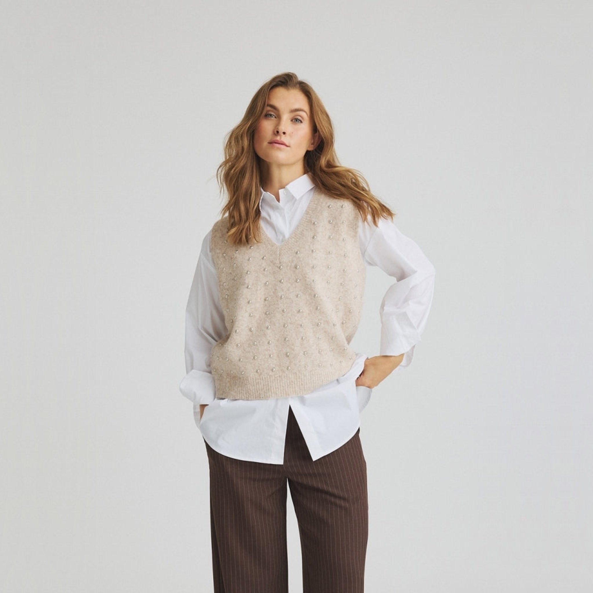Model i beige vest med perler foran, båret over en hvid skjorte