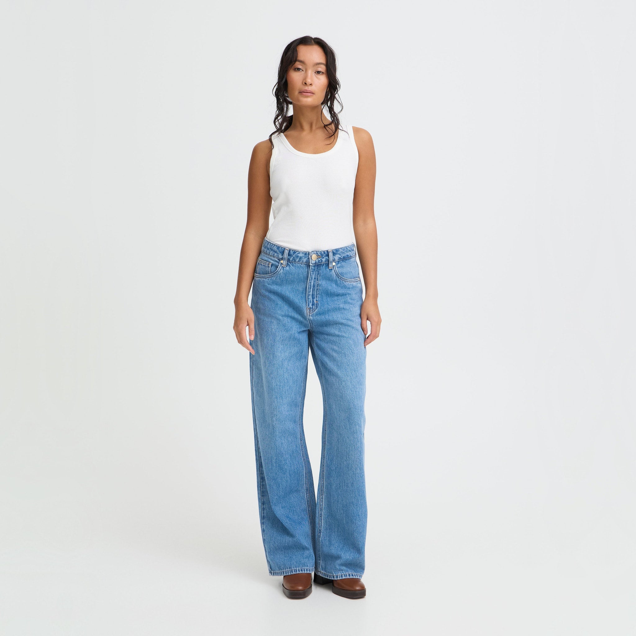 Model i blå April wide leg jeans med høj talje, stylet med hvid tanktop og brune støvler