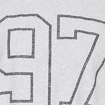 Nærbillede af tallet 97 lavet af små sorte sten på grå t-shirt