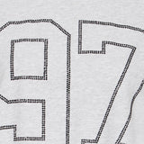 Nærbillede af tallet 97 lavet af små sorte sten på grå t-shirt